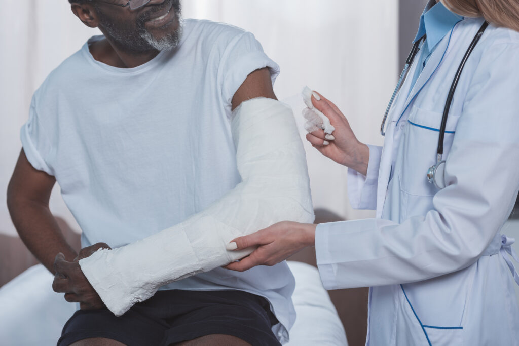 Cropped image of doctor bandaging african american patient hand with plaster cast