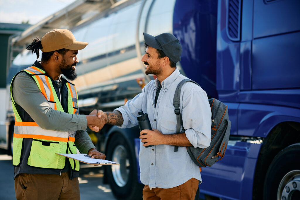 Happy truck driver and African American freight transportation manager handshaking on a parking lot.