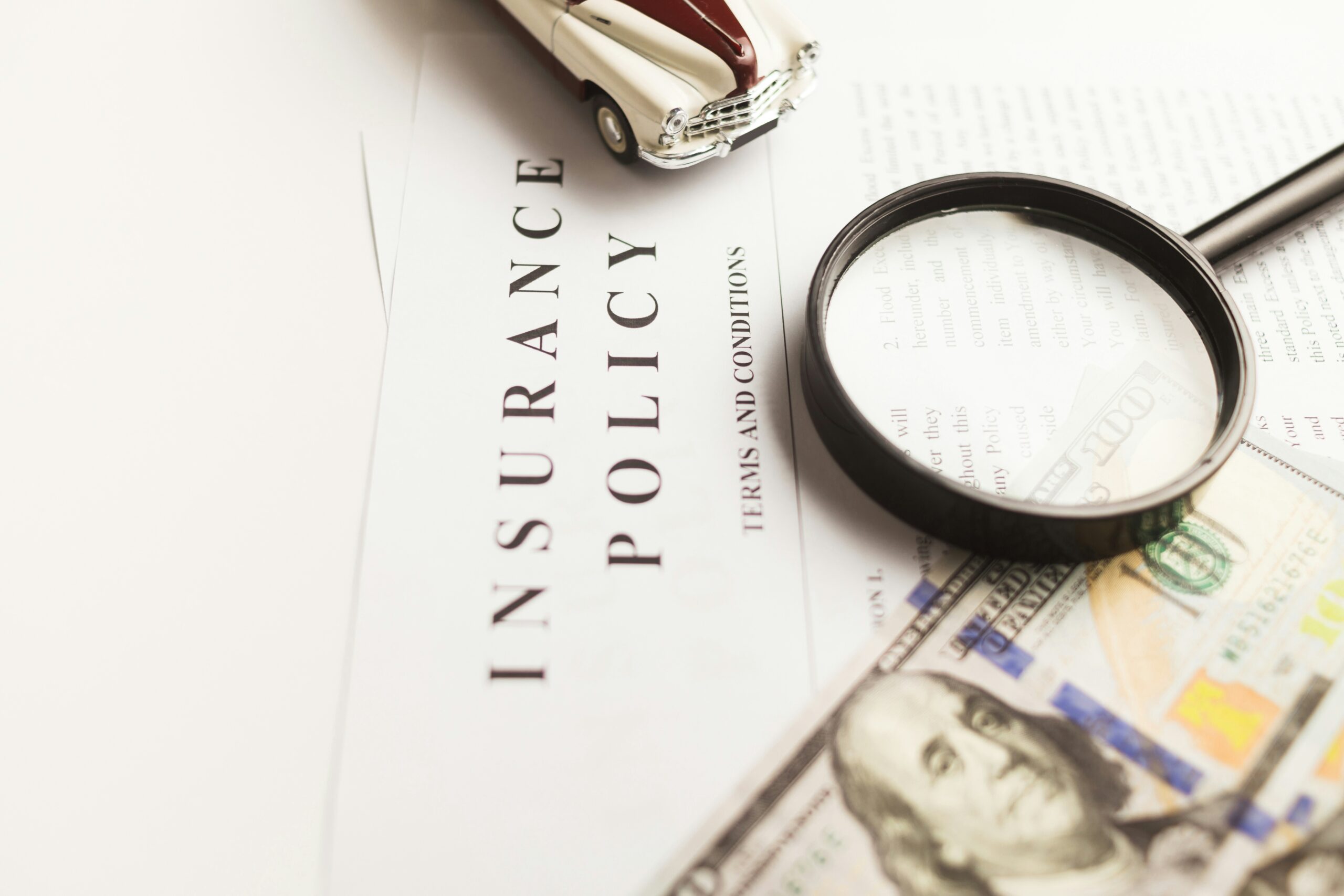 A magnifying glass, a hundred dollar bill and an insurance paper